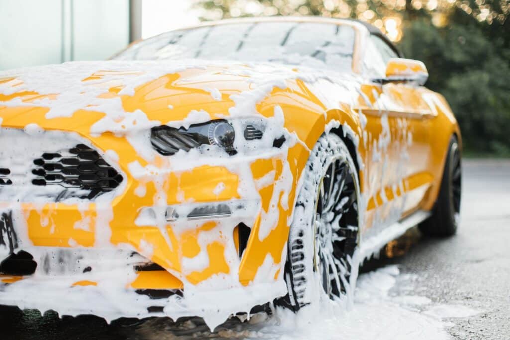 Car enthusiast in Birmingham using the two-bucket washing method to clean a vehicle, reducing scratches and improving maintenance efficiency.