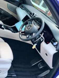 Interior view of a modern car with a sleek design. The dashboard features a large touchscreen infotainment system and a digital instrument cluster. The steering wheel has multiple controls and a keychain is hanging from the ignition. The seats are light-colored leather.