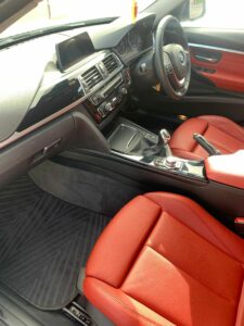 Interior of a modern car showing the front seats, dashboard, and center console. The dashboard features a digital display and various controls. The seats are upholstered in red leather, and the interior overall has a black and red color scheme.