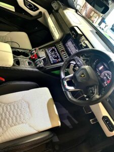 Interior view of a luxury car showcasing a sleek dashboard, advanced touchscreen controls, and a sporty steering wheel with a prominent logo. The seats feature a stylish combination of light and dark upholstery with honeycomb patterns.